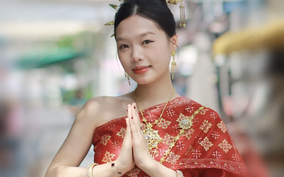 A woman in traditional Thai dress greeting with a wai